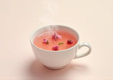 Steaming cup of pink rose tea with floating petals